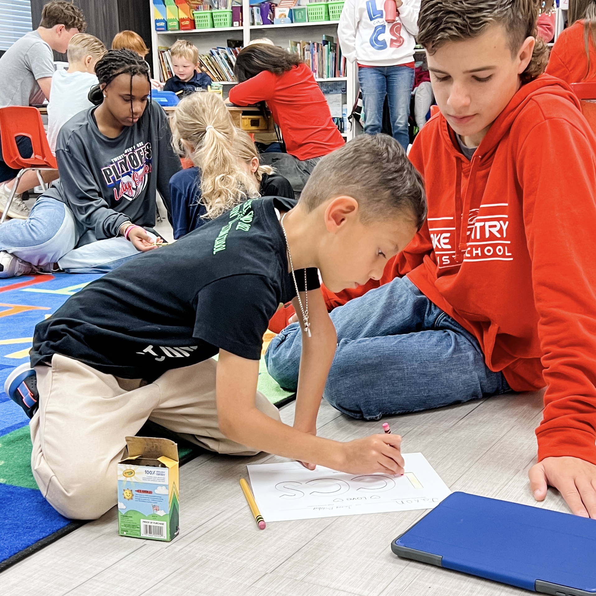 Middle school students working with elementary students, sitting on the floor filling out Bible Buddies curriculum.